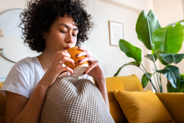 Young African American woman blowing on hot tea to cool beverage off. Relaxing at home sitting on the couch drinking coffee. Copy space. Lifestyle concept.